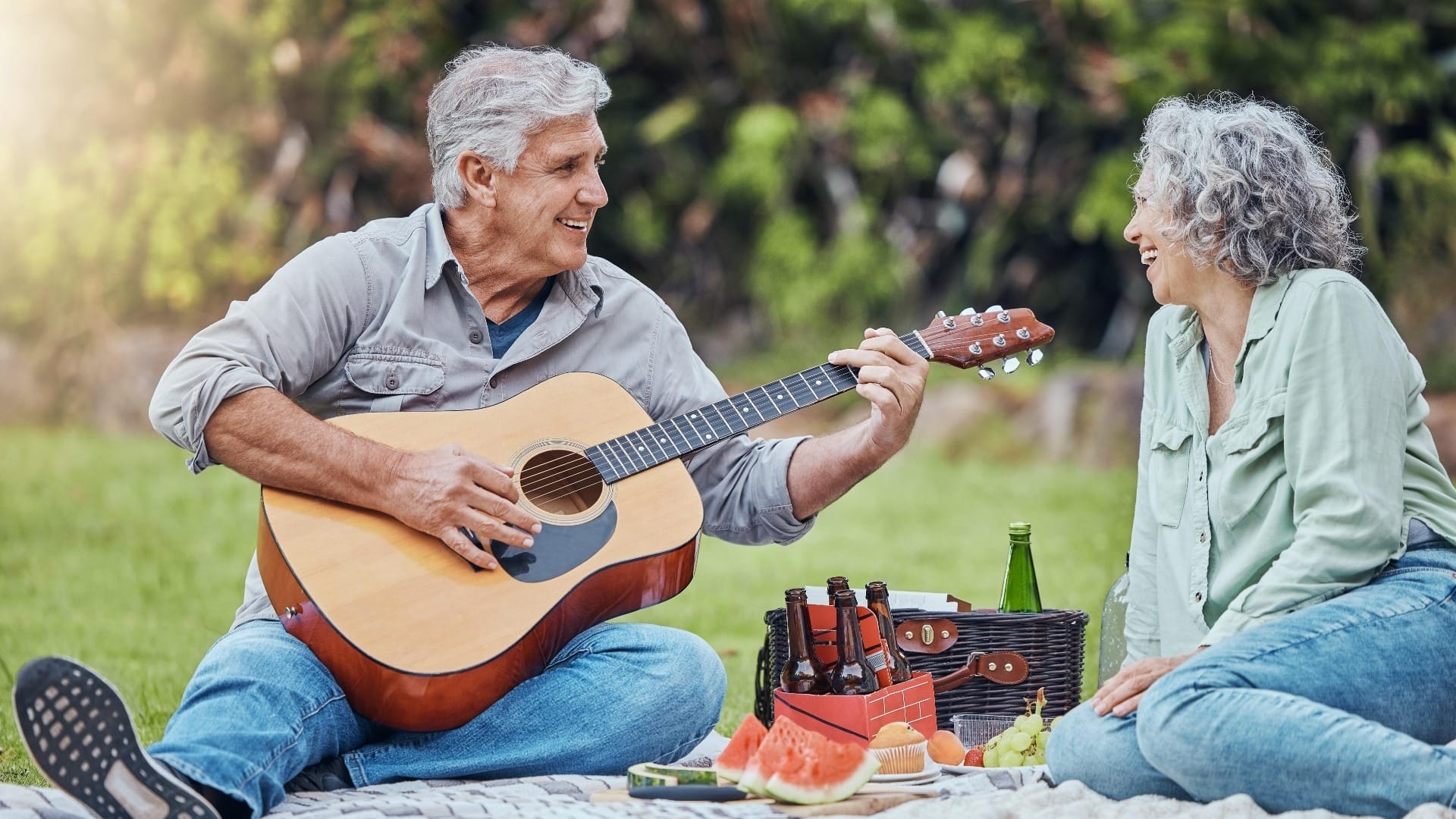 Retirement, love and guitar with couple on picnic in park together for relax, summer or food. Nature, wellness and happy old man and woman listening to music in countryside field for health in spring
